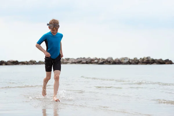 Guapo adolescente chico corriendo en neopreno traje de baño en el mar — Foto de Stock