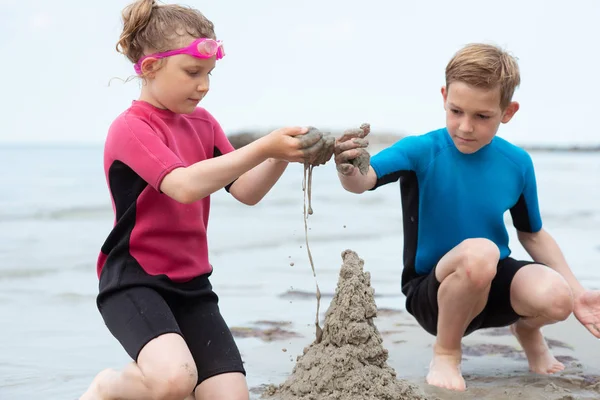 Two happy siblings children in neoprene swimsuits playing with s — Stock Photo, Image