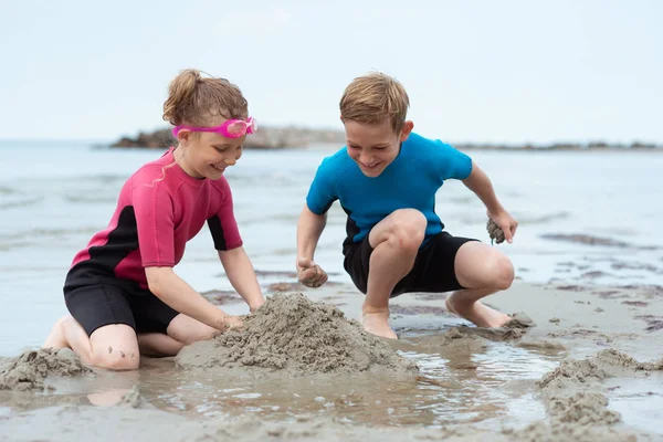 Due fratelli felici bambini in costume da bagno in neoprene giocare con s — Foto Stock