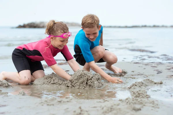 Two happy siblings children in neoprene swimsuits playing with s — Stock Photo, Image