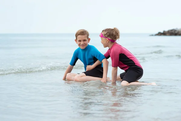 Zwei glückliche Geschwisterkinder in Neopren-Badeanzügen spielen mit s — Stockfoto