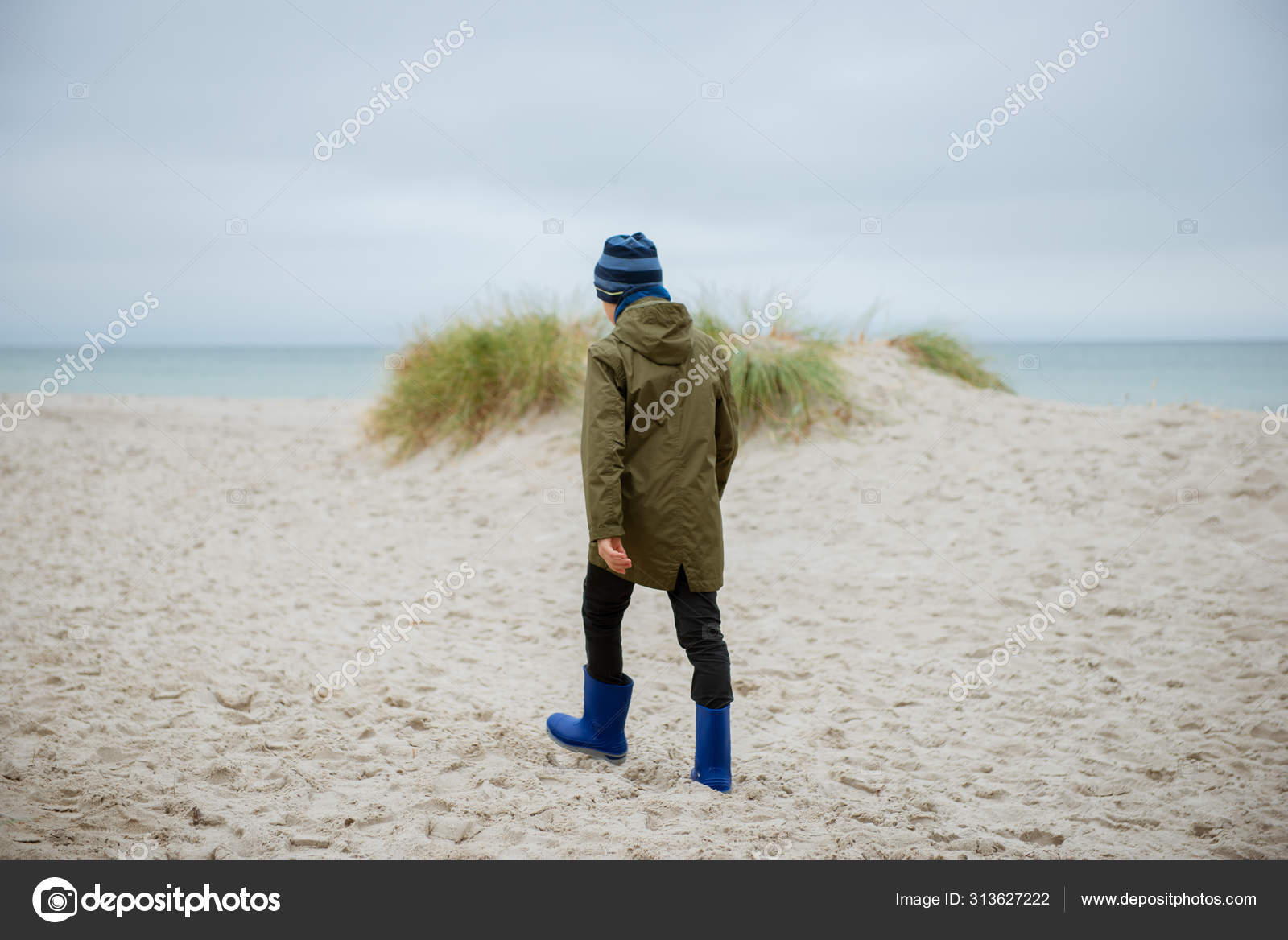 Teen boy in rain jacket and high rubber boots walking in sand du Stock