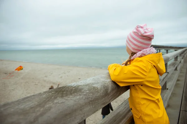 Portrait of little girl in yellow jacket on wooden pier at rainy — Stock Photo, Image