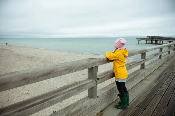 Porträt eines kleinen Mädchens in gelber Jacke auf einem Holzsteg bei regnerischem Wetter — Stockfoto