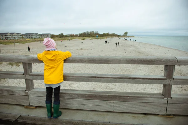 Porträtt av liten flicka i gul jacka på träpir vid regnigt — Stockfoto