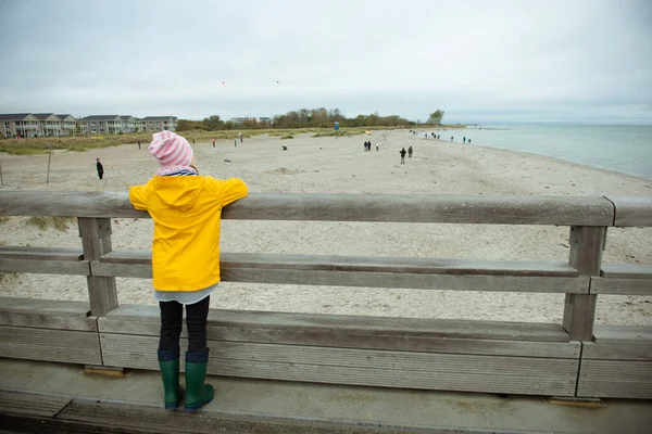 Retrato de niña en chaqueta amarilla en muelle de madera a la lluvia — Foto de Stock