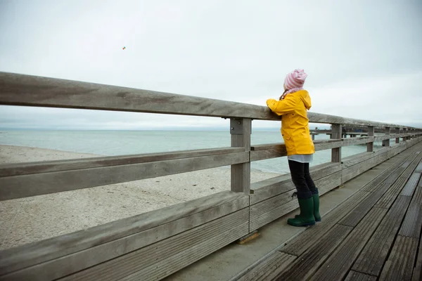 Portrait of little girl in yellow jacket on wooden pier at rainy — Stock Photo, Image