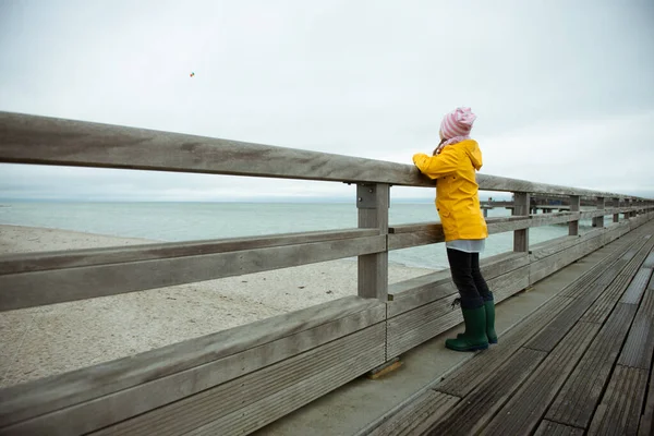 Porträt eines kleinen Mädchens in gelber Jacke auf einem Holzsteg bei regnerischem Wetter — Stockfoto