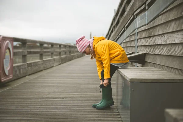 Ritratto di bambina in giacca gialla su pontile di legno a pioggia — Foto Stock