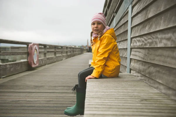 Portrait of little girl in yellow jacket on wooden pier at rainy — Stock Photo, Image