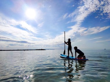 Neoprene takımlı mutlu genç çocuklar Baltık denizinde SUP sörf tahtasında ve kürek çekerken eğleniyorlar.