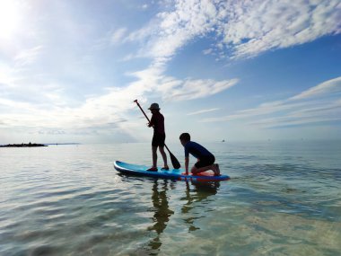 Neoprene takımlı mutlu genç çocuklar Baltık denizinde SUP sörf tahtasında ve kürek çekerken eğleniyorlar.