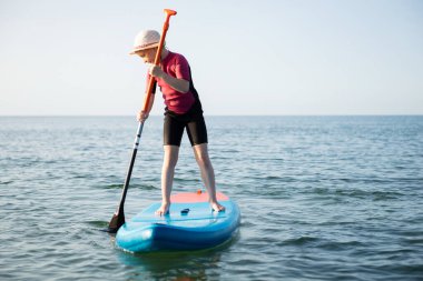 Happy teen child girl paddling on sup board in Baltic sea clipart