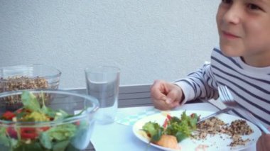 İki mutlu genç çocuk, aileleriyle sohbet edip yemek yiyorlar. Sıcak arka bahçenin terasında sağlıklı bir akşam yemeği yiyorlar.