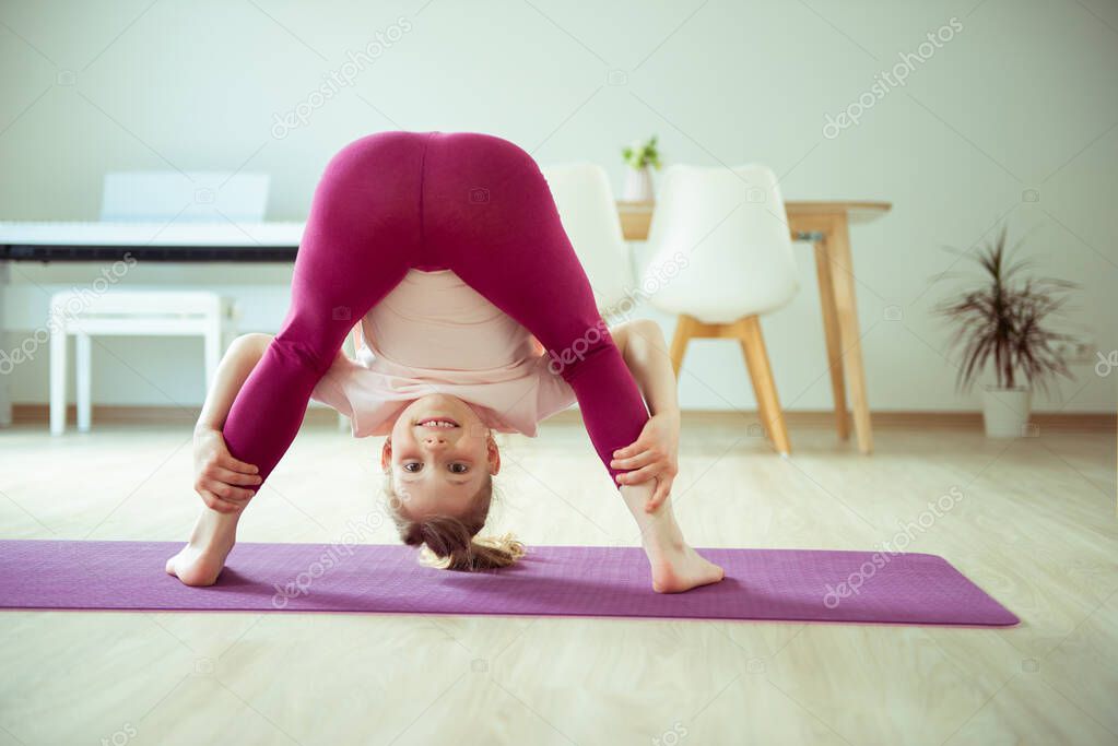 Pretty happy child girl having fun making yoga exercises at home 