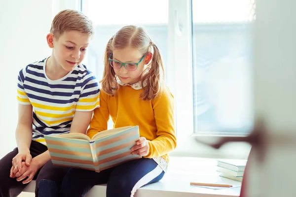 二つの幸せな十代の子供たちは机の上に座って楽しい本を読んで休日 — ストック写真