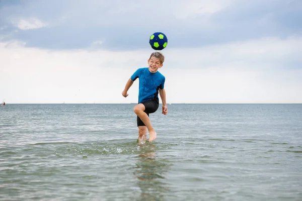 ハッピーハンサムなティーン男の子実行していますととともにボールでネオプレン水着でバルト海 — ストック写真