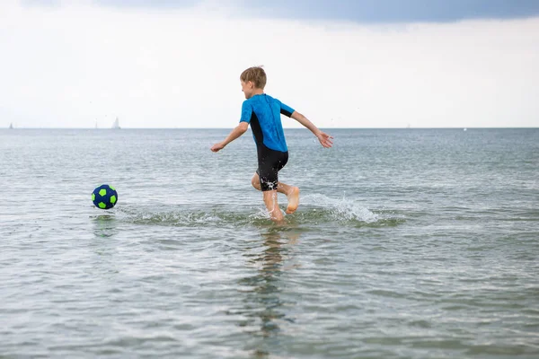 ハッピーハンサムなティーン男の子実行していますととともにボールでネオプレン水着でバルト海 — ストック写真