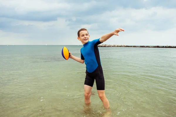 ハッピーハンサムなティーン男の子実行していますととともにボールでネオプレン水着でバルト海 — ストック写真