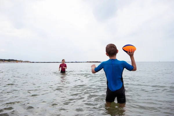 二人の幸せな兄弟子供遊びとジャンプでボールで水でネオプレンスーツでバルト海 — ストック写真
