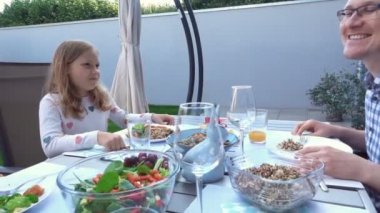 İki mutlu genç çocuk, aileleriyle sohbet edip yemek yiyorlar. Sıcak arka bahçenin terasında sağlıklı bir akşam yemeği yiyorlar.