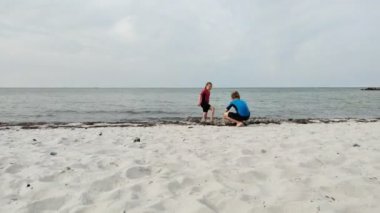 Neoprene mayo giymiş iki mutlu çocuğun Baltık Denizi 'ndeki kumsalda eğlenip oyun oynamalarının videosu.