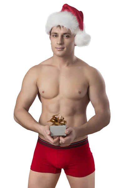 Ein nackter, gut aussehender, muskulöser Mann mit Weihnachtsmannmütze, der eine Geschenkbox hält, ist — Stockfoto