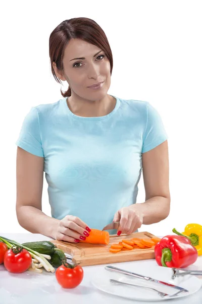 Beautiful female looking at camera slicing carrot near the table — Stock Photo, Image