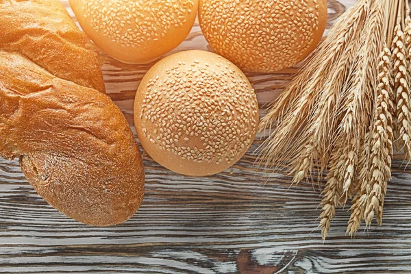 Long loaf bread wheat ears on wooden surface