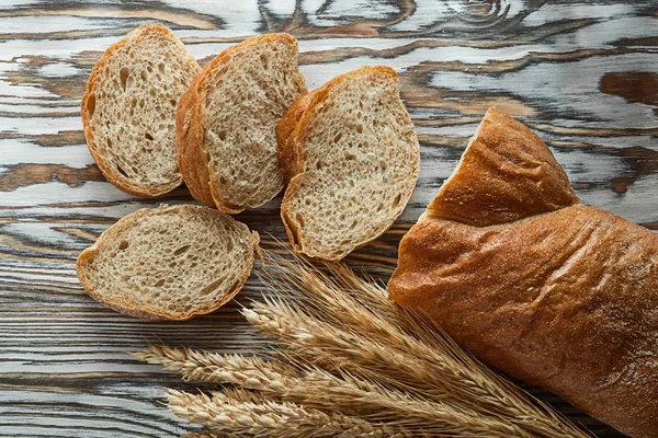 Crusty sliced bread wheat ears on wooden surface