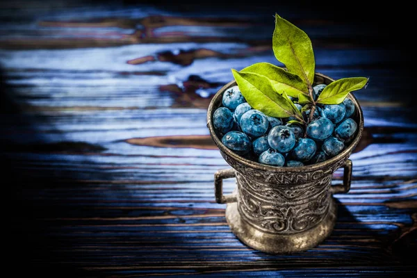 Yaban mersini yeşil metal kapta vintage ahşap tahta üzerinde yapraklar.