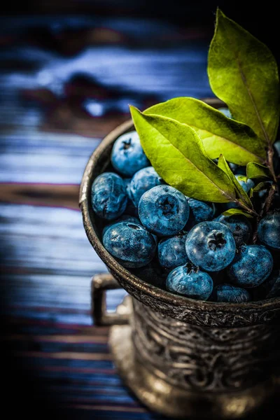 Huckleberries yeşil metal kapta vintage ahşap tahta üzerinde yapraklar..