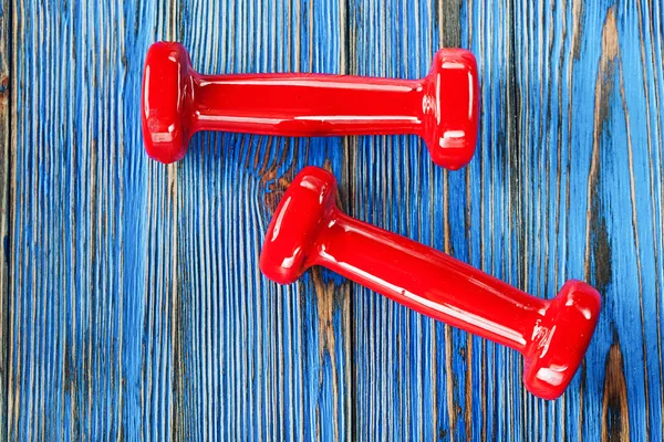 Pair of red fitness dumbbells on vintage wooden board.