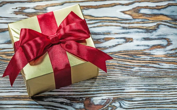 Caja de regalo de oro con lazo rojo sobre tabla de madera —  Fotos de Stock