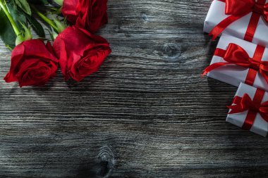 Ahşap tahta üzerinde kırmızı gül beyaz hediye kutuları.