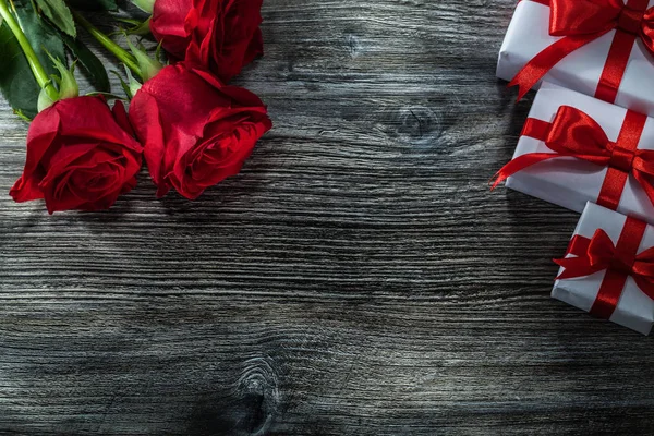 Ahşap tahta üzerinde kırmızı gül beyaz hediye kutuları.