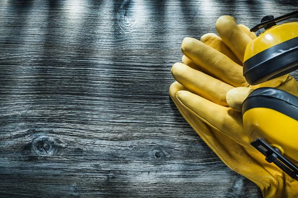 Pair of safety gloves earmuffs on wooden board.