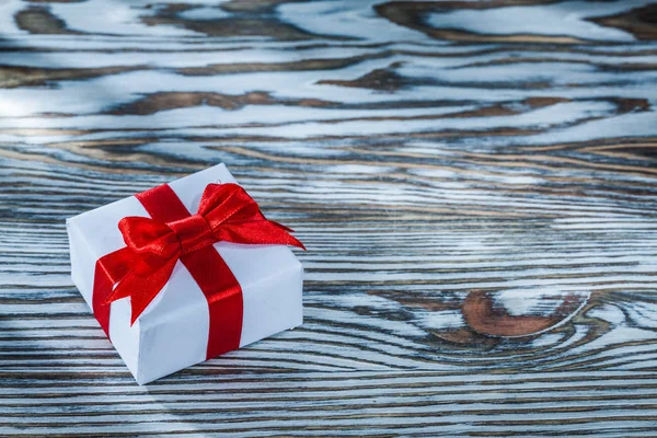 Red present box with knot on wooden background.