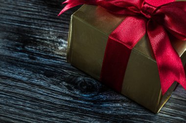 Ahşap üzerinde kırmızı kurdele ile altın hediye kutusu.