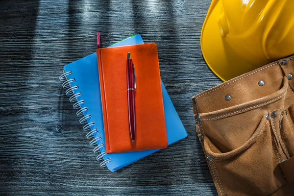 Notebooks pen safety cap leather tool belt on wooden board.