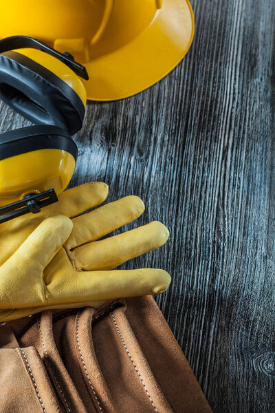 Protective gloves building helmet earmuffs tool belt on wooden board.