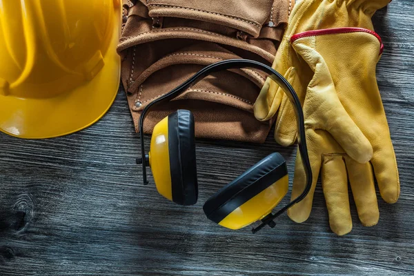 Leather safety gloves cap tool belt earmuffs on wooden board.