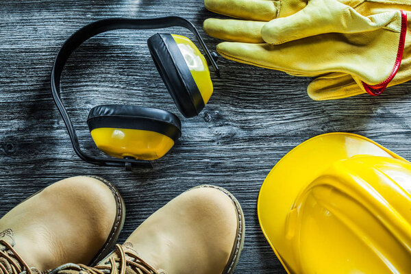 Earmuffs protective gloves safety cap boots on wooden board.