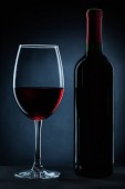láhve a sklenice na víno s červeným vínem na černém