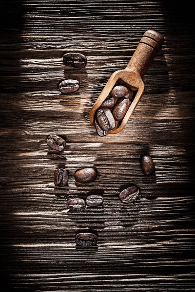 Roasted coffee crops in scoop on vintage wooden board.