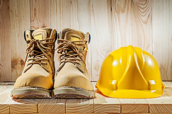 Bottes de travail et casque jaune sur fond de bois — Photo