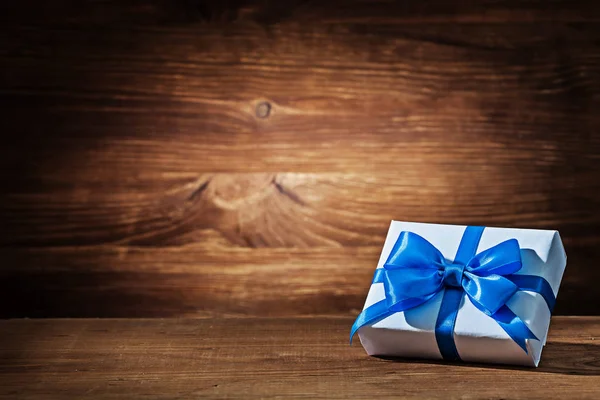 Antika ahşap üzerine mavi kurdele ile beyaz hediye kutusu — Stok fotoğraf
