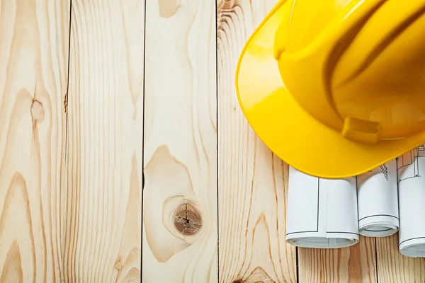 Rolled blueprints and yellow construction helmet on wood boards — Stock Photo, Image