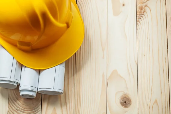 Żółty kask budowlany i białe walcowane plany na drewnianych — Zdjęcie stockowe