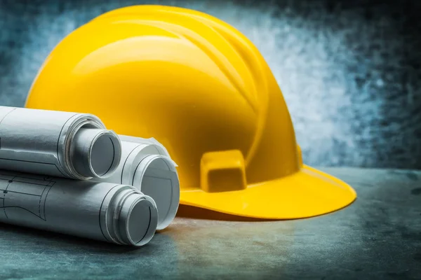 Rolls of blueprints and yellow construction helmet on metalic ba — Stock Photo, Image